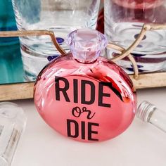 a pink bottle with the words ride or die painted on it next to some glasses