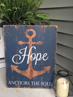 a wooden sign that says hope anchors the soul next to a candle and potted plant