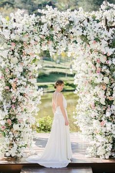 a woman in a wedding dress standing under an arch of flowers