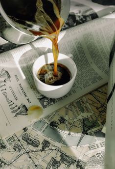 a person pouring coffee into a white cup on top of a newspaper with maps in the background