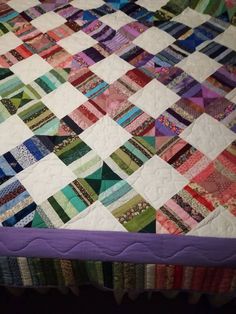 a quilt is laying on top of a bed with purple trimmings and colorful squares