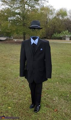 a man in a suit and tie with a hat on his head standing in the grass