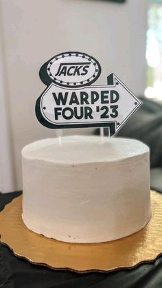 a white cake sitting on top of a wooden table next to a black and white sign