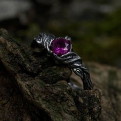 a ring with an amethorate stone in the middle sitting on top of a rock