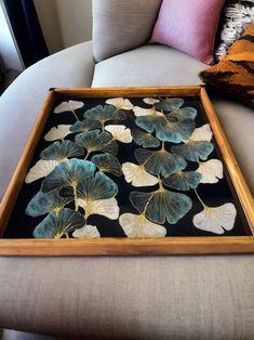 a wooden tray with blue and white flowers on it sitting on a couch next to pillows