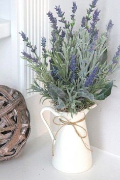 a white pitcher filled with purple flowers on top of a table next to a wicker basket