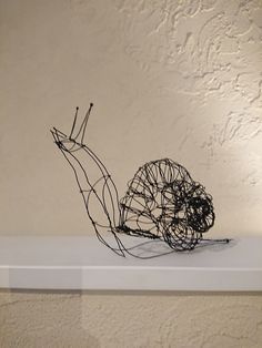 a wire sculpture of a snail sitting on top of a white shelf next to a wall