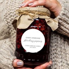 a person holding a jar of jam with a label that says, sandy's homemade thanksgiving preserves