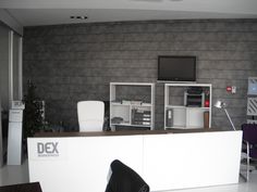 an office with a desk, chair and television on the wall behind it in front of a gray brick wall