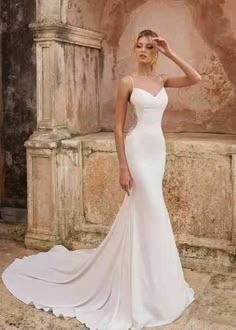 a woman in a white wedding dress standing on a stone wall with her hands behind her head