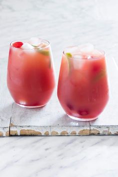 two glasses filled with drinks sitting on top of a marble counter next to each other