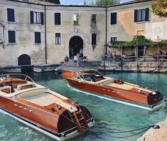 two wooden boats tied to the dock in front of an old building with people on it