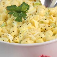 a white bowl filled with macaroni and cheese covered in parsley next to a spoon