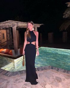 a woman standing in front of a pool at night wearing a black dress with cutouts