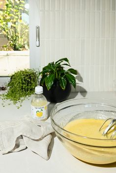 a glass bowl filled with yellow liquid next to a potted plant on a counter