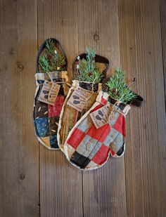 three oven mitts are sitting on a wooden surface with pine branches in the middle