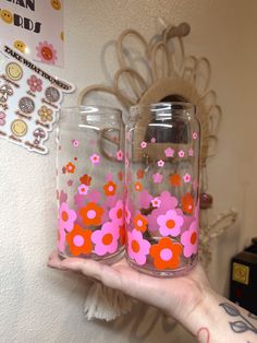 a person holding two glass jars with flowers painted on the inside and one in the middle