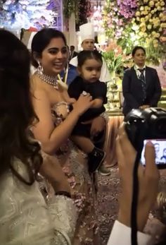 a woman in a wedding dress is holding a baby and taking a photo with her camera