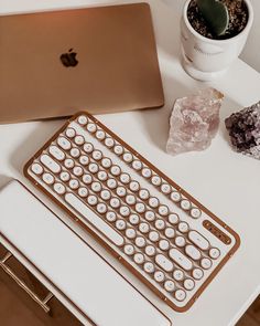 an apple laptop computer sitting on top of a white desk next to a keyboard and some rocks