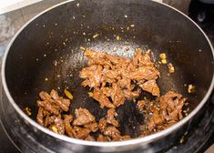 beef is cooking in a wok on top of the burner with other food items