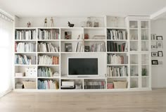 a living room filled with lots of white bookshelves and a flat screen tv