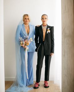 two women standing next to each other in front of a white wall wearing blue and black outfits