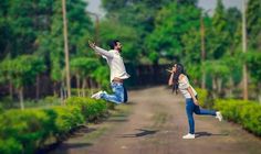 two people jumping in the air on a dirt road with trees and bushes behind them