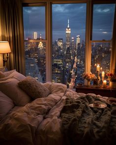 a bedroom with a large window overlooking the city lights and candles are lit on the bed