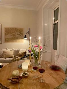 a wooden table topped with two glasses of wine and candlelight candles next to a couch