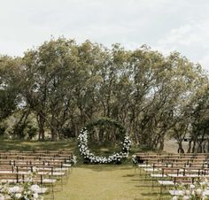 an outdoor ceremony setup with white flowers and greenery on the aisle, surrounded by trees