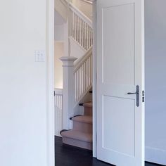 an open door leading to a staircase in a white room with hardwood floors and stairs