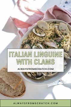 a white bowl filled with pasta and clams on top of a table next to bread