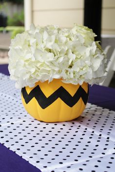 a yellow vase filled with white flowers on top of a purple and black table cloth