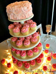 a three tiered cake with pink frosting on top and cupcakes below