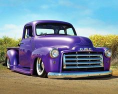 an old purple truck parked on the side of a road