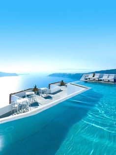 an empty swimming pool with chairs and tables on the edge, overlooking water that looks like it is floating in the ocean