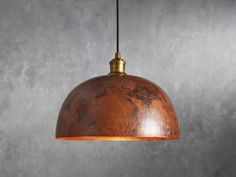 a wooden light fixture hanging from a metal wire on a gray wall with concrete walls in the background