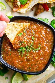 a hand holding a tortilla chip and dipping it into a bowl filled with salsa