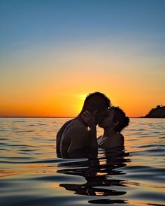 a man and woman kissing in the water at sunset, with an island in the background