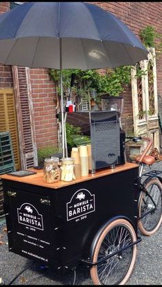 an old fashioned ice cream cart on the side of a road with a black umbrella over it