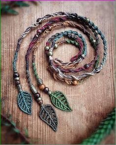 a necklace with beads and leaves on it sitting on top of a wooden table next to plants