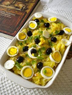 a casserole dish with eggs and olives in it next to a book