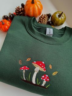 machine embroidered sweatshirt featuring a cute mushroom scene with falling leaves colours pictured are sand and forest green embroidered onto a gildan sweatshirt, composed of 50% cotton and 50% polyester sizing as follows Sizes: S (50,8cm-68,6cm) / M (55,9cm-71,1cm) / L (61cm-73,7cm) / XL (66cm-76,2cm) / XXL ( 71,1cm-78,7cm) these are made to order and i may need to order your preferred size & colour, so please allow time for your sweatshirt to be ready!  if you have any questions or would like Mushroom Scene, Autumn Leaf Color, Cute Mushroom, Gildan Sweatshirt, Mushroom Design, Creative Embroidery, Leaf Coloring, Falling Leaves, Gildan Sweatshirts