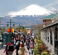 many people are walking down the street in front of a snow - capped mountain,