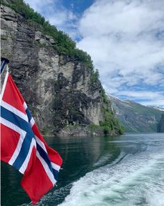 the norwegian flag is flying high over the water on a boat in front of some cliffs