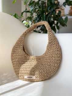 a woven purse sitting on top of a white table next to a potted plant