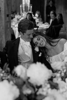 a man and woman sitting at a table with flowers in front of them on their wedding day