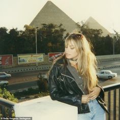 a woman standing on top of a balcony next to a building with a pyramid in the background