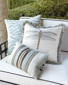 some pillows are sitting on a white bench with a dragonfly pillow in the middle