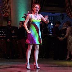 a woman in a multicolored dress is standing on stage with her hands out